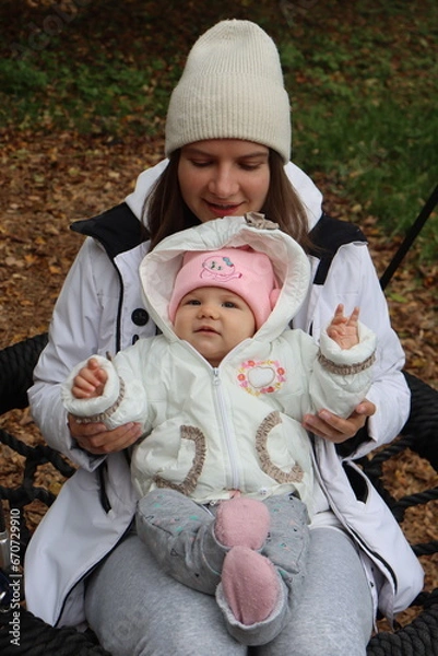 Obraz mother holds a little girl in her arms and rides on a swing in the park in autumn