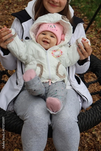 Obraz mother holds a little girl in her arms and rides on a swing in the park in autumn