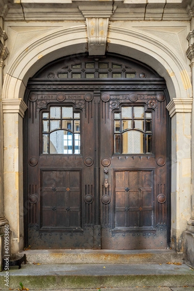 Fototapeta Large wooden arched gates with lots of detailing, set into a stone wall. At the top of the gate is the inscription, anno domini 1903