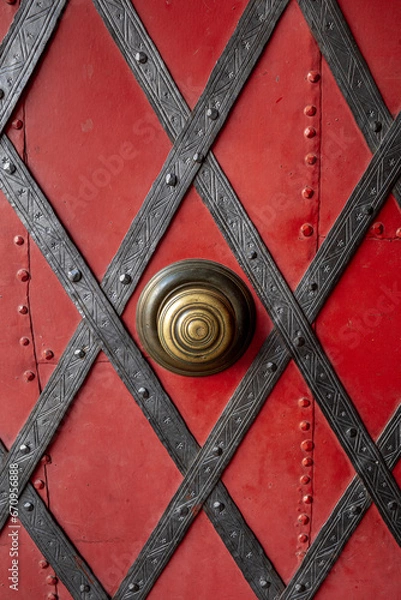 Fototapeta Close up of an old metal red door with diagonal iron decorative strips and rivets.