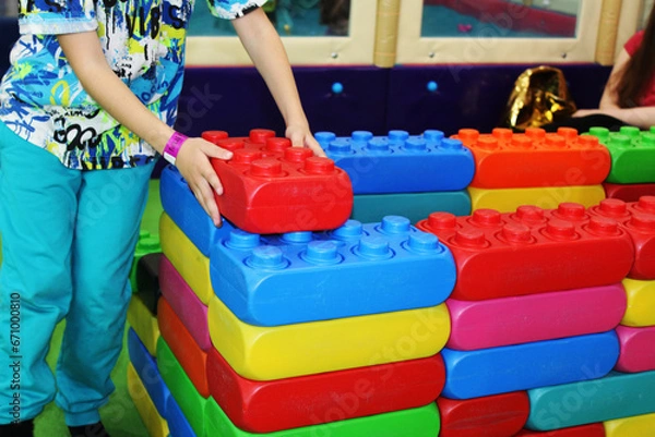 Fototapeta the child's hands build a wall of toy building blocks of different colors