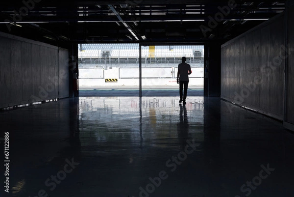 Obraz Silhouettes of a man entering a race car racing circuit paddock.