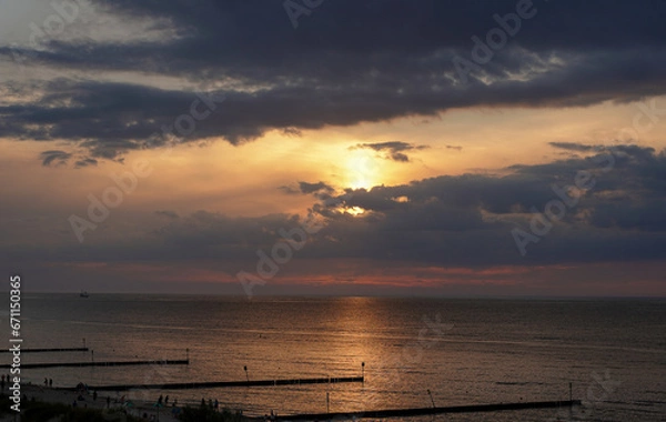 Fototapeta View of the setting sun over the calm sea under a cloudy sky.
