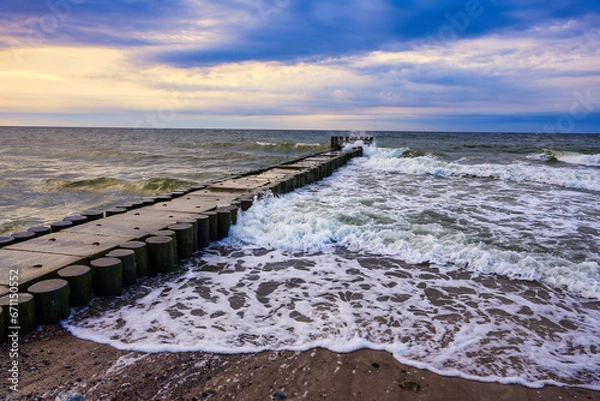 Fototapeta High and turbulent sea waves crash and break against the massive breakwater.