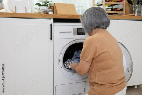 Obraz back view senior woman doing laundry with washing machine at home