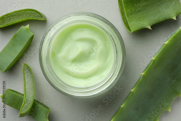 Fototapeta Jar with cream and cut aloe leaves on light grey background, flat lay