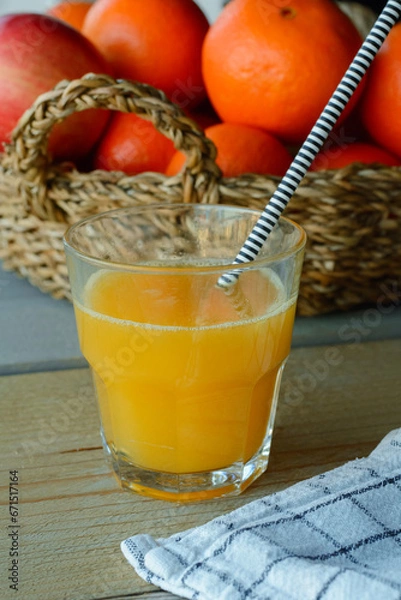 Obraz One glass of orange juice is standing on the wooden table with a basket of oranges in the background. Eating healthy every day. Orange juice and oranges