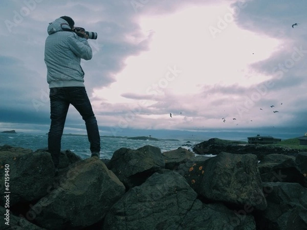 Fototapeta Photographer over rocks shooting seagulls by the sea