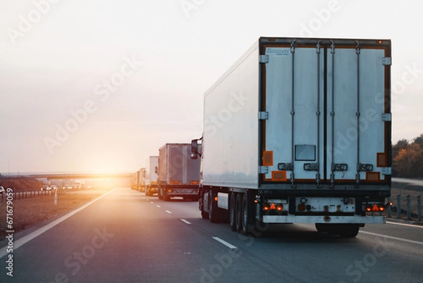 Fototapeta Modern white semi-trailer trucks on the highway driving in the right lane. Commercial vehicle for shipping and post delivery. Shipping of the goods on land with a door-to-door delivery process.