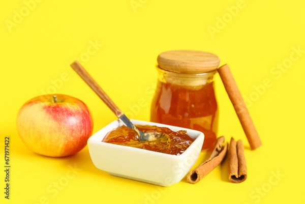 Fototapeta Jar and bowl of sweet apple jam with cinnamon on yellow background