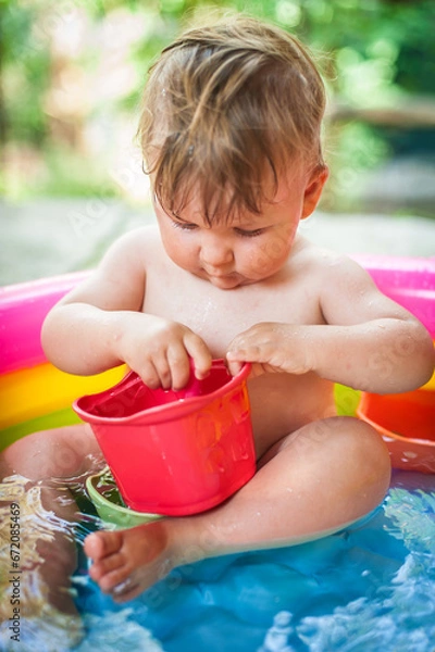 Fototapeta A cute little baby boy is playing with toys while bathing in a little colorful wading pool. Summer time. Joy and happiness concept. Love and family emotion