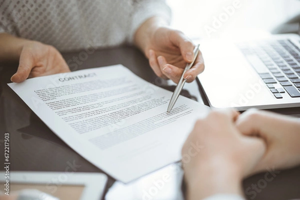 Fototapeta Business people sitting and discussing contract in office, closeup. Partners or lawyers working together at meeting before signing papers. Teamwork and partnership