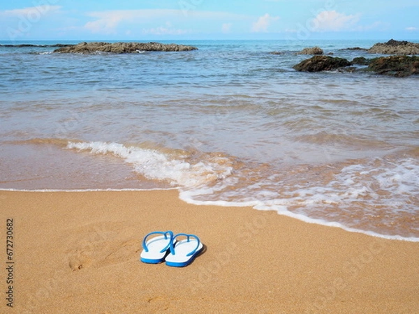 Fototapeta White flip flop on the Sandy Beach.Sandals on sandy beach with a small wave in front of the sea. Tourists take off sponge shoes were removed and left in wet sand. Concept Relax in holiday
