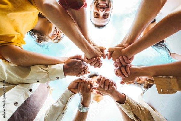 Fototapeta Multi ethnic group of young people holding hands outdoors - Community life style concept with guys and girls hugging together outside - Unity, support and collaboration concept