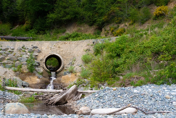 Fototapeta An image of a large concrete culvert running under a rural road way and diverting waste water runoff.
