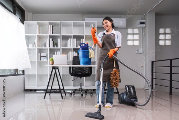 Fototapeta An Asian housewife uses a telephone to communicate with her employer. During cleaning in the office