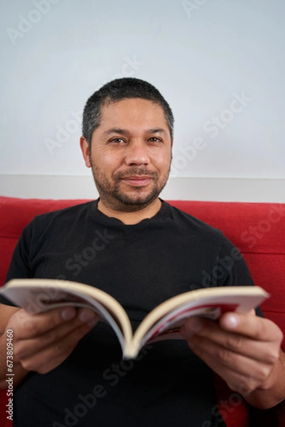 Obraz Man on Sofa Holding Book, Engaging with Camera