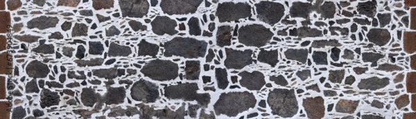 Fototapeta Kanarische Mauer aus grauem vulkanischem Gestein in weißem Verputz, am Rand eingefasst mit braunen Steinen