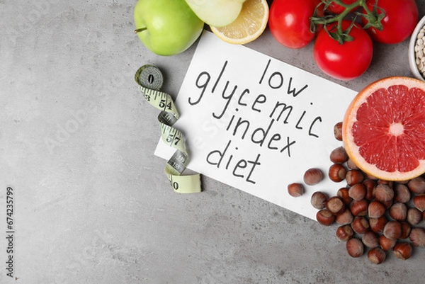 Obraz Paper with words Low Glycemic Index Diet, measuring tape and food on grey table, flat lay. Space for text