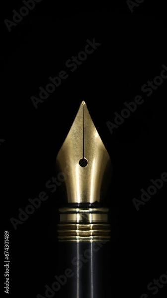 Fototapeta closeup macro shot of the gold tip of a luxury fountain ink pen used for calligraphy isolated in a black background