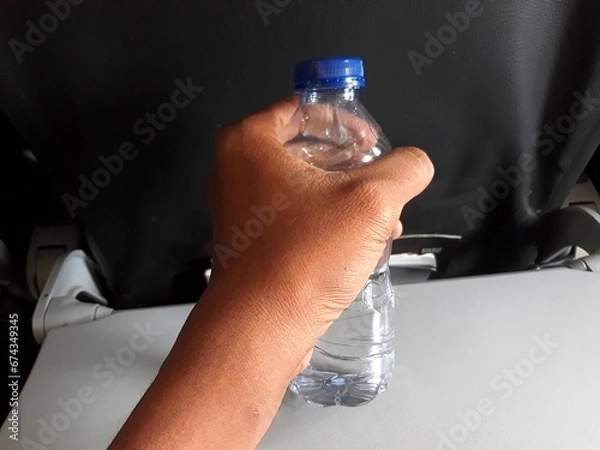 Obraz selective focus hand holding mineral water bottle above airplane flight cabin desk