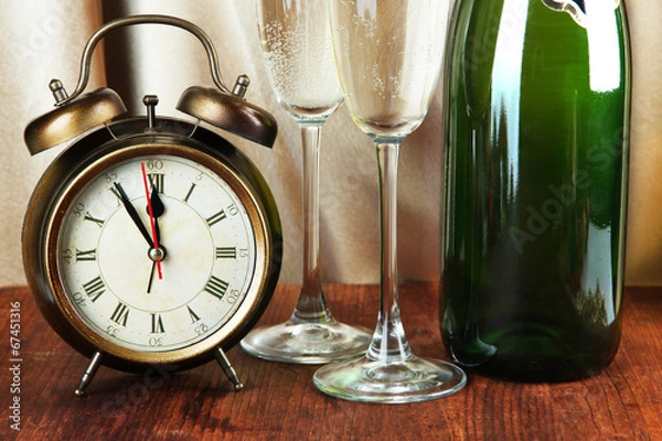 Fototapeta Alarm clock with champagne on table on golden cloth background
