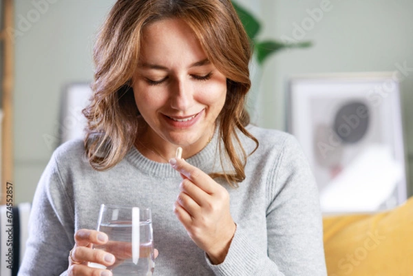 Fototapeta Happy young woman taking vitamins