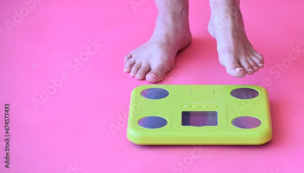 Fototapeta Caucasian bare feet standing on scale to measure weight,pink background. Control of weight, dieting and overweighting. 