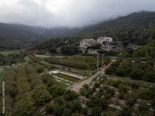 Fototapeta Aerial View of Hazelnut Grove with Farmhouses, Forest, and Misty Mountains in 'Bosquet,' Tarragona"
