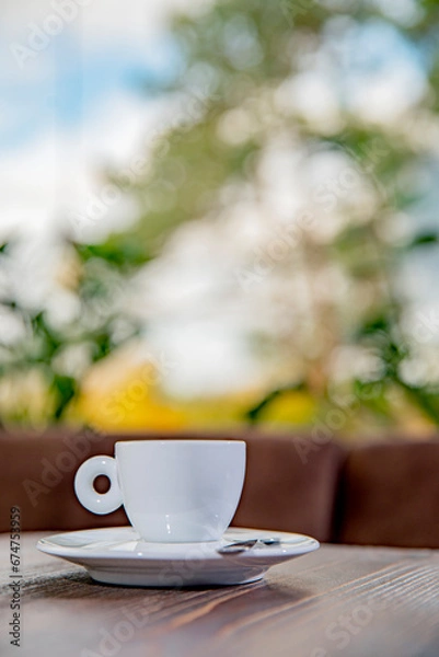 Obraz cup of coffe standing on plate on wooden table, colourful trees in the background