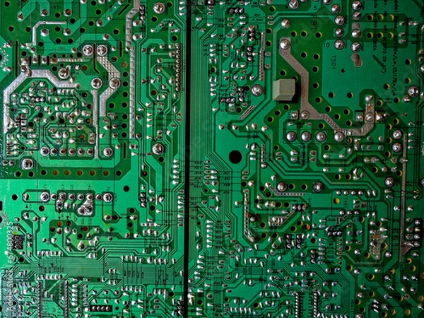 Fototapeta A close-up reveals the intricacies of a green computer circuit board, with various silver and gold components adorning its surface, resembling a technological landscape.