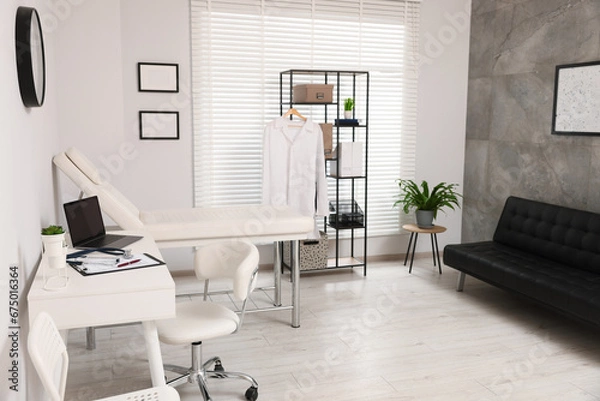 Fototapeta Modern medical office with doctor's workplace and examination table in clinic