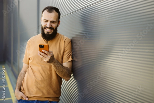 Obraz Caucasian bearded man smiling using smartphone