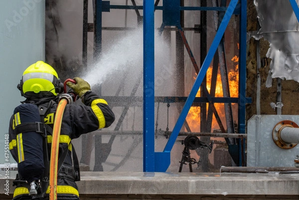 Fototapeta Firefighter with a breathing apparatus uses water to extinguish a fire of flammable liquids in a chemical factory