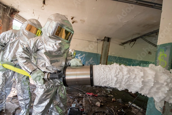 Fototapeta Firefighters in special protective suits against heat spray extinguishing foam used to extinguish flammable liquids