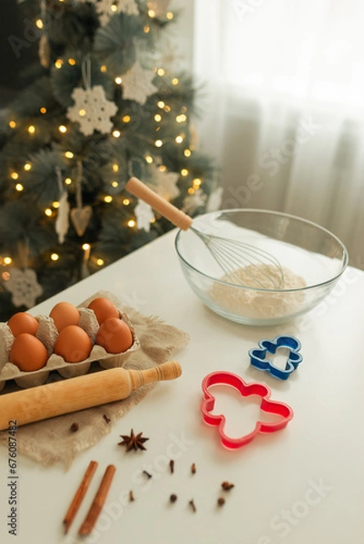 Fototapeta On the kitchen table there is a bowl with flour, a whisk, spices and molds for making Christmas cookies