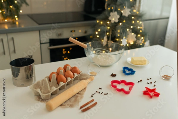 Fototapeta On the kitchen table there is a bowl with flour, a whisk, spices and molds for making Christmas cookies