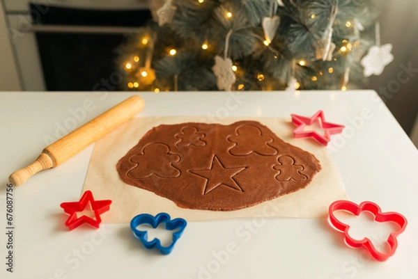 Fototapeta Rolled out dough lies on parchment paper with molds and rolling pin for cutting