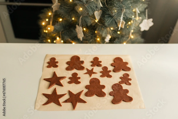 Fototapeta Cut out shapes from Christmas cookie dough lie on parchment paper