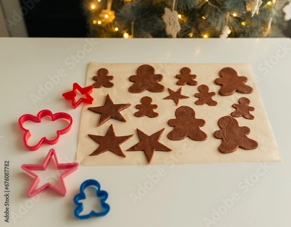 Fototapeta Cut out shapes from Christmas cookie dough lie on parchment paper