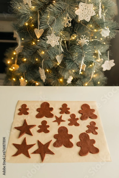 Fototapeta Cut out shapes from Christmas cookie dough lie on parchment paper