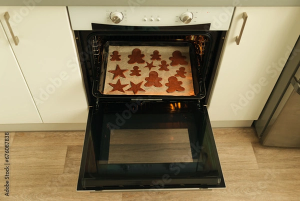 Fototapeta Cut out Christmas cookie dough shapes lie on a baking sheet in the oven