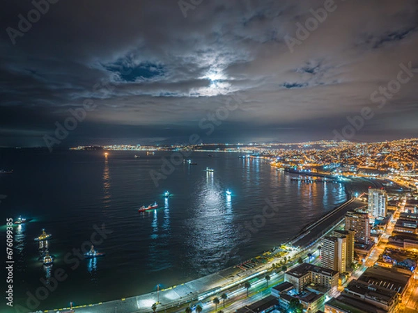 Fototapeta Vista aérea noturna da região do Terminal Pacífico Sur Valparaíso com lua cheia escondida entre nuvens e barcos ao redor.
