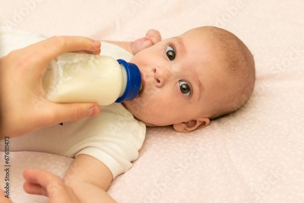 Fototapeta The baby drinks milk from a bottle. Feeding the baby with infant formula.