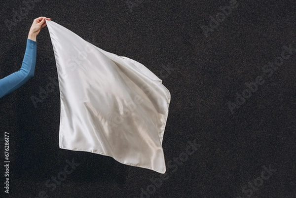 Fototapeta White silk scarf in woman's hand floating on the wind on dark grey background. Lifestyle.