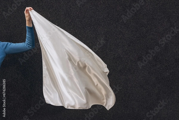 Fototapeta White silk scarf in woman's hand floating on the wind on dark grey background. Lifestyle.