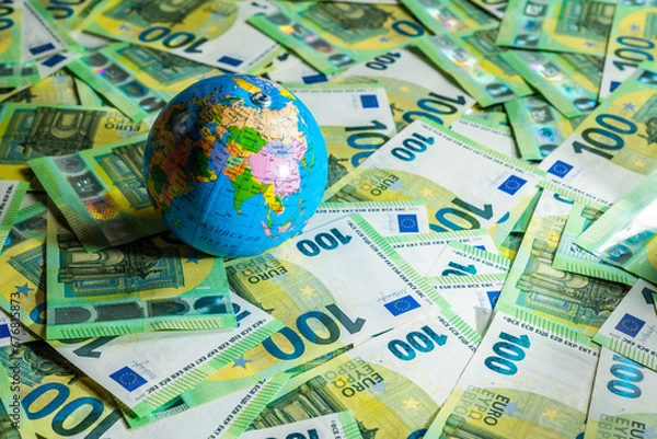 Fototapeta A little globus with shadow placed on many money bills, 100 euros mixed up