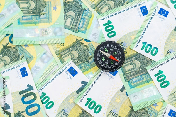 Obraz  Top view on a little black compass with red arrow on many euro money bills, financial choices concept