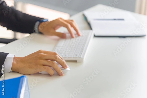Fototapeta Closeup of male hand clicking wireless digital mouse working with desktop computer at office desk