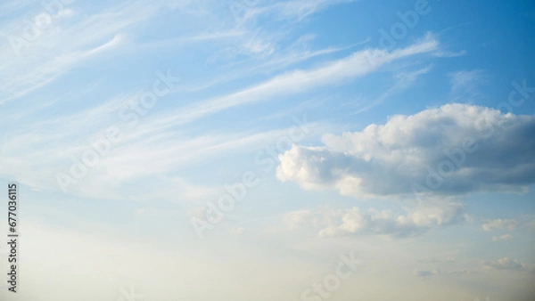 Fototapeta The wind was blowing the fluffy white clouds across the bright blue sky, creating a motion in the atmosphere.